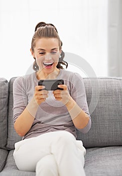 Surprised young woman sitting on sofa and reading sms