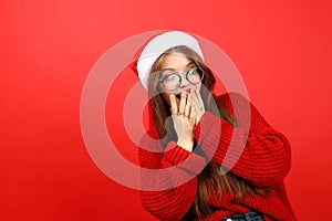 Surprised young woman in sweater and santa hat on red background