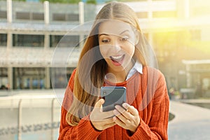 Surprised young woman using smart phone outdoors