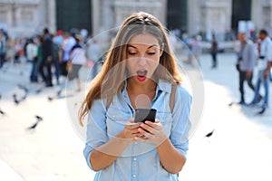 Surprised young woman using smart phone outdoors. Close up portrait surprised screaming girl looking at phone seeing news or