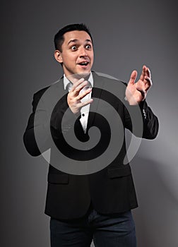 Surprising  grimacing  and gesturing the hands man looking in black suit with funny face on grey studio background. Closeup