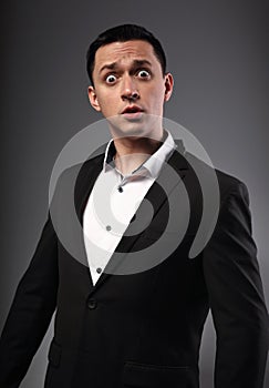 Surprising  grimacing man looking in black suit with funny face on grey studio background. Closeup