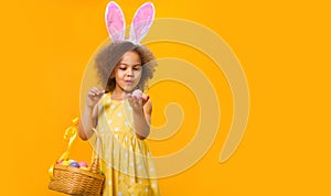 A surprized Black girl with rabbit ears on her head with a basket of colored eggs in her hands