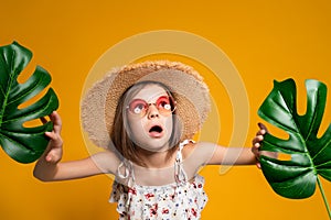 Surprized little girl in glasses and a straw hat on a yellow background in the studio