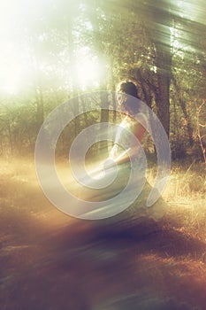 Surreal blurred background of young woman sitting on the stone in forest.