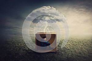 Surreal concept with a scared guy shelters inside a cardboard box. Introvert man caged by own fears as a thunderstorm cloud