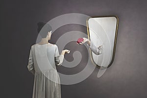 Surreal gesture of a hand coming out of the mirror to give a rose to a woman