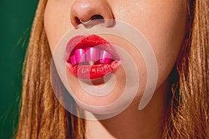 Surreal image for beauty salon. Cropped female face with painted nails inside mouth against green background.