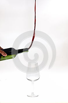 Surreal image of red wine pouring out of a bottle towards the top instead of the glass over white background