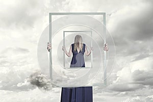 Surreal image of a woman holding a frame that reflects herself