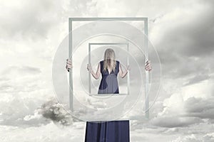 Surreal image of a woman holding a frame that reflects herself photo