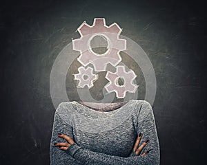 Surreal image young woman with crossed armss and gear symbol instead of head drawn over blackboard background. Business cogwheels