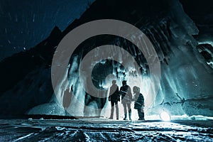 Surreal landscape with people exploring mysterious ice grotto cave. Outdoor adventure. Family exploring huge icy cave