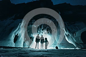 Surreal landscape with people exploring mysterious ice grotto cave. Outdoor adventure. Family exploring huge icy cave