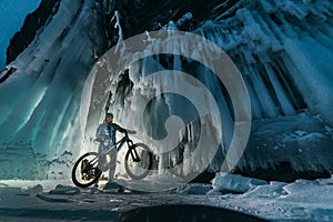 Surreal landscape with woman exploring mysterious ice grotto cave. Outdoor adventure bike. Girl exploring huge icy cave