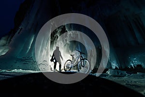 Surreal landscape with woman exploring mysterious ice grotto cave. Outdoor adventure bike. Girl exploring huge icy cave