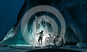 Surreal landscape with woman exploring mysterious ice grotto cave. Outdoor adventure bike. Girl exploring huge icy cave