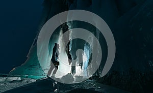 Surreal landscape with woman exploring mysterious ice grotto cave. Outdoor adventure. Girl exploring huge icy cave, dark