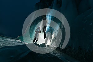Surreal landscape with woman exploring mysterious ice grotto cave. Outdoor adventure. Girl exploring huge icy cave, dark