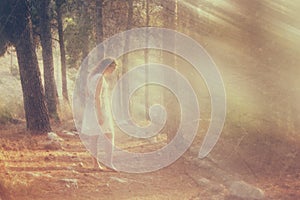 Surreal photo of young woman standing in forest. image is textured and toned. dreamy concept.