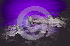 Surreal purple moody and spooky seascape with rocks and hazy waters