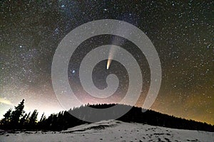 Surreal view of night in mountains with starry dark blue cloudy sky and C/2020 F3 NEOWISE comet with light tail