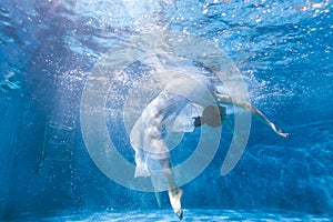 Surreal woman dances in the pool under the water.