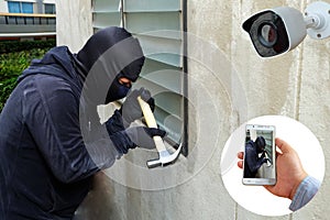 Surveillance Camera capture and record caught Masked thief with hammer and hand holding Mobile Phone Detecting on application