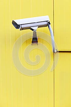 Surveillance camera on the exterior sandwich wall of a yellow building.