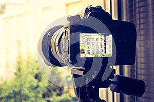 Surveillance and stalking concept: Camera with telephoto lens on tripod, observing a house