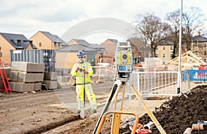 Surveyor builder site engineer with theodolite total station at construction site outdoors during surveying work