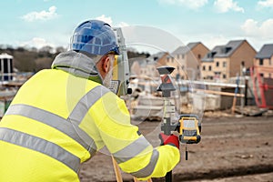 Surveyor builder site engineer with theodolite total station at construction site outdoors during surveying work