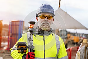 Surveyor builder site engineer with theodolite total station at construction site outdoors during surveying work