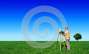 Surveyor on green field. Blue sky in background.