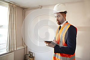 Surveyor In Hard Hat And High Visibility Jacket With Digital Tablet Carrying Out House Inspection photo