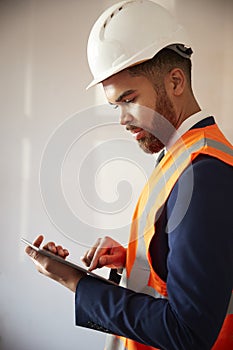 Surveyor In Hard Hat And High Visibility Jacket With Digital Tablet Carrying Out House Inspection