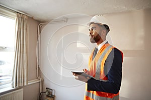 Surveyor In Hard Hat And High Visibility Jacket With Digital Tablet Carrying Out House Inspection