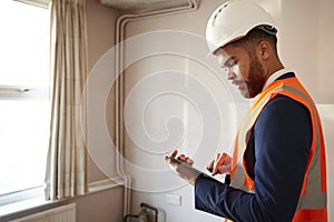 Surveyor In Hard Hat And High Visibility Jacket With Digital Tablet Carrying Out House Inspection photo