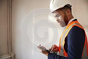 Surveyor In Hard Hat And High Visibility Jacket With Digital Tablet Carrying Out House Inspection