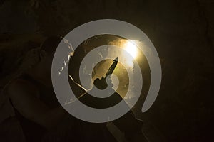 Survival man with knife backlit in dusty cave