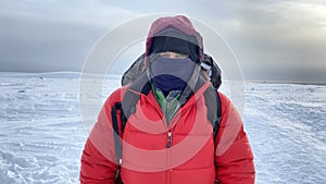 Survival in the north. A man in warm clothes with a backpack behind his back looks at the camera. Close-up on the eyes. Winter