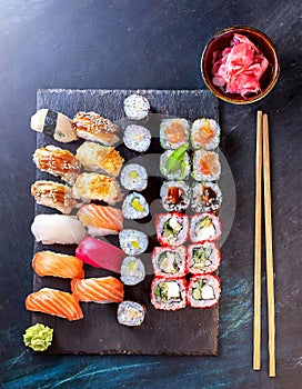 Sushi assortment platter of rolls, maki, nigiri, sashimi on dark stone board with sticks