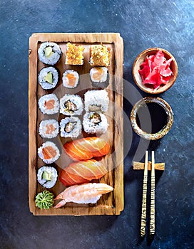 Sushi assortment platter of rolls, maki, nigiri, sashimi on wood board with sticks and soy sauce