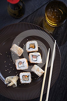 Sushi on a brown plate with a glass of beer, soy sauce and natural wooden chopsticks..