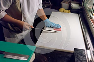 Sushi chef slicing a raw fresh fish with a sharp knife on a whit