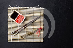 Sushi chopsticks, soy sauce, ginger, bamboo mat and empty plate on black background.