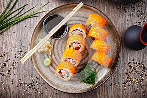 Sushi maki rolls California Futomaki with salmon, avocado, cucumber, crab and flying fish roe on a plate with chopsticks