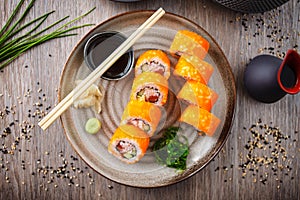 Sushi maki rolls California Futomaki with salmon, avocado, cucumber, crab and flying fish roe on a plate with chopsticks