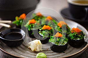 Sushi maki rolls with crab, seaweed salad and flying fish roe on a plate with chopsticks, soy sauce, wasabi and ginger