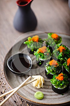 Sushi maki rolls with crab, seaweed salad and flying fish roe on a plate with chopsticks, soy sauce, wasabi and ginger